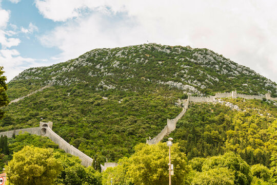 A mountain with a historical stone wall of Ston city winding up its slope under a cloudy sky, Ston, Croatia