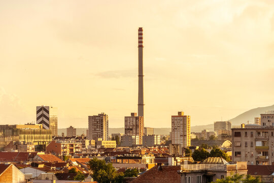 Sunset over Zagreb city skyline with a tall industrial chimney and residential buildings against a cloudy sky, Zageb, Croatia