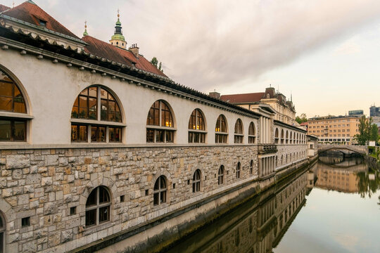 Sunset reflections on a serene Ljubljana  river beside a historic stone market building with arched windows, Ljubljana, Slovenia