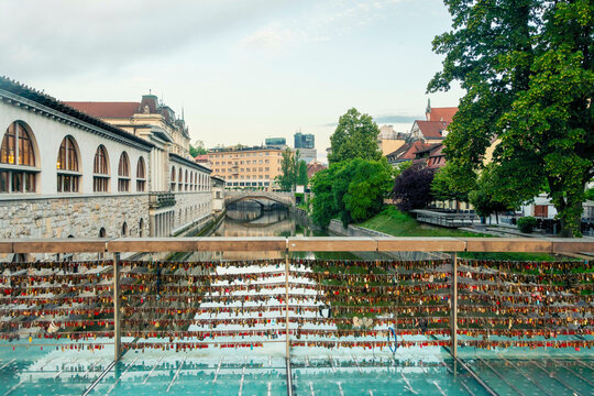 Scenic view of a bridge with numerous love locks attached to the railing, a traditional building to the left, and the cityscape of Ljubljana in the background under a blue sky, slovenia
