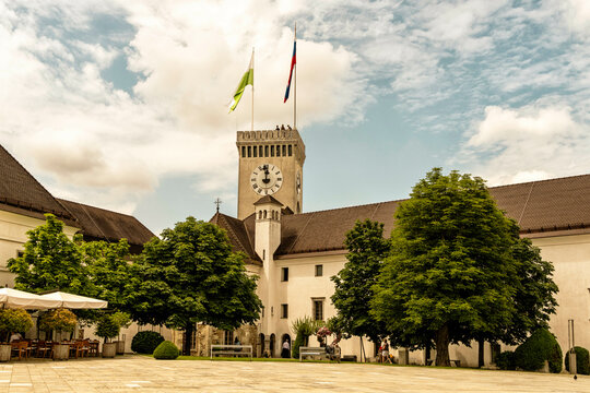 A sunny day at historic Ljubljana castle courtyard with a clock tower, lush green trees, and some visitors enjoying the outdoors, Ljubljana, Slovenia