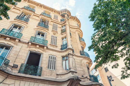 Elegant Parisian  or provencial building with wrought iron balconies under a clear blue sky, flanked by green trees, Marseille, France