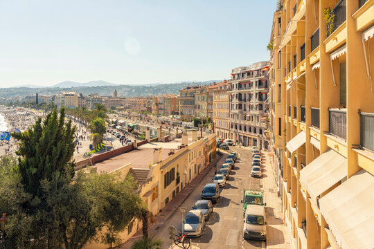 Sunny day view of a European city street lined with colorful buildings, parked cars, and a glimpse of the waterfront in the distance, Nice, FRance