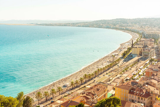 Aerial view of a bustling beach alongside cityscape of Nice with clear blue waters and a sunny sky in summer