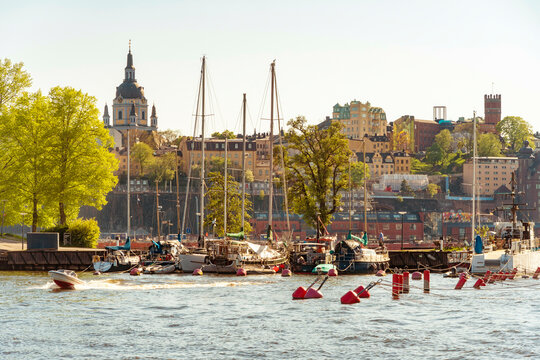 A scenic view of a harbor with boats and a vibrant cityscape in the background under clear blue skies with Slussen and Sodermalm island, Stockholm, Sweden