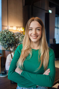 Smiling young woman in a green top standing with arms crossed in an indoor setting, Berlin, Germany