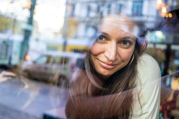 Smiling woman seen through a window with city reflections overlaying her face, Berlin, Germany