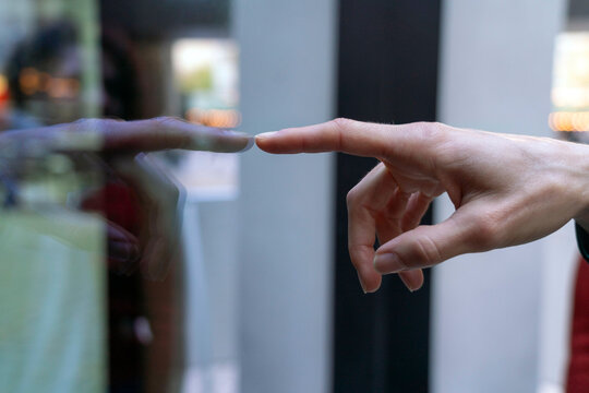 Close-up of a person's hand reaching out to touch a glass surface with a reflection visible, Berlin, Germany