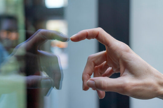 Close-up of a person's hand reaching out to touch a glass surface with a reflection visible, Berlin, Germany