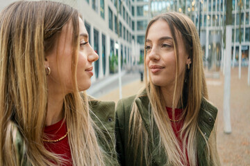 Woman in green jacket smiling while her reflection appears on a glass surface, with a modern building facade in the background, Berlin, Germany