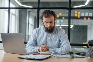 Front view, by laptop. Businessman is working in the office