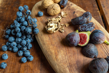 Autumn fruits and nuts (grapes, figs, prunes, walnuts) on wooden platter on wooden chest