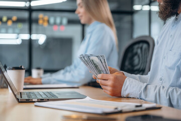 Currency in hands, counting. Man and woman are in the office together