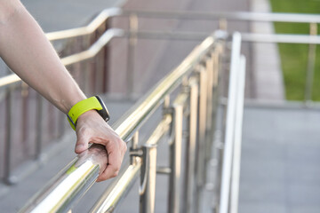 Close up of caucasian adult male hand holding rail with green smartwatch wristband outdoors.