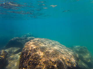 Sunlight filters through the water, illuminating a large rock formation on the seabed.