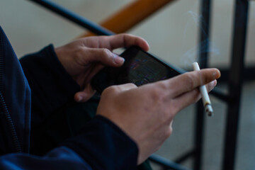 close-up of a man's hand holding a smartphone and cigarette