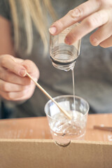 Young caucasian female mixing resin in a cup using a wooden stick for craft projects.