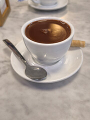 white cup of chocolate with saucer, spoon and wafer on a table