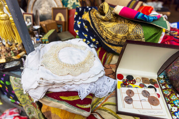 Vintage embroidery, pearl necklace, buttons in a box, and silk scarves for sale at a flea market.