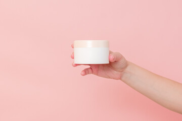 Hand holding jar of cosmetic cream on pink background. Cosmetics beauty mockup for product branding