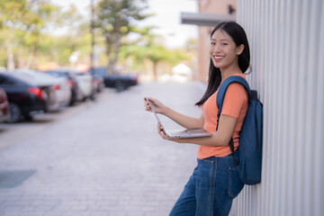 Young Asian student holding a laptop and smiling brightly in the university parking lot after class on a sunny day, enjoying the vibrant campus atmosphere and embracing her academic journey © MINAE