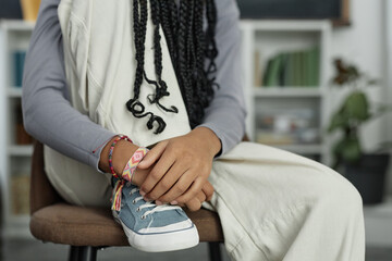 Close up detail shot of Black teenage girl wearing canvas shoes and colorful handmade friendship bracelets sitting on chair with leg up copy space