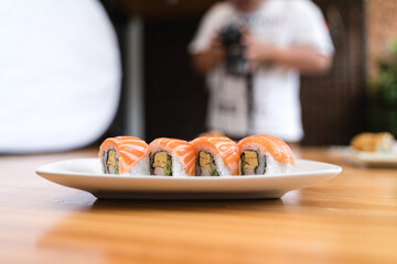 Fresh salmon sushi rolls on a white plate during a professional food photoshoot session with blurred background elements.