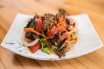 A vibrant dish of crispy fish skin salad with fresh vegetables and a tangy dressing on a decorative plate.