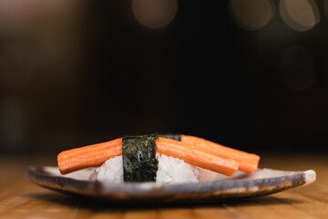 Close-up of kani sushi with nori wrap on rice, artistically presented on a ceramic plate with a dark blurred background.