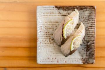 Sushi topped with tender fish slices and garnished with citrus peel on a rustic ceramic plate.