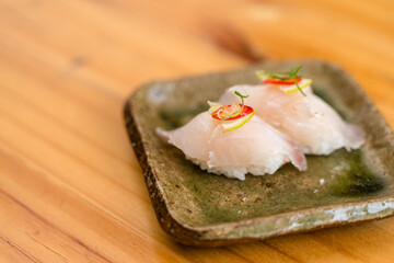 Delicate white fish sushi topped with citrus and chili slices, served on a rustic green ceramic plate.