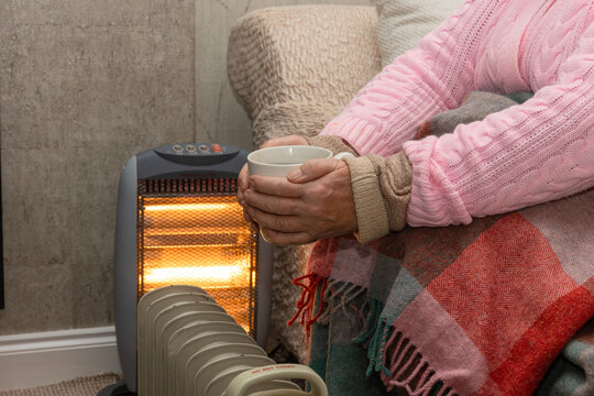 Pensioner lady keeping warm during cold spell, January 2025 with layered clothing, electric heaters and warm drink. In 2024 the newly elected Labour Government changed the winter fuel allowance policy