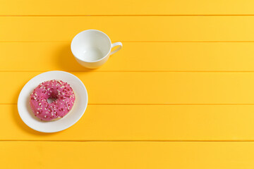 Empty White Coffee Cup and Pink Glazed Donut on a Yellow Wooden Background