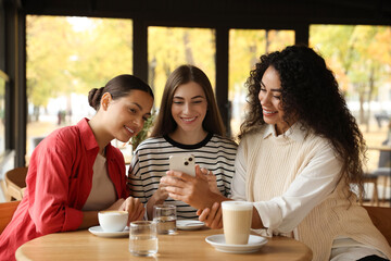 Women using smartphone while having coffee in cafe