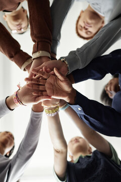 Vertical from below shot of group of children stacking hands and huddling during team building exercise in school focus on palms