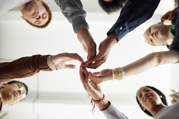 From below shot of group of children touching hands during team building exercise in school or at support group session copy space