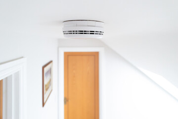 Ceiling view of a newly installed smoke detector seen on the first floor of a new show home. Doors...