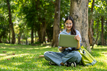 A young woman sits in the grass with a laptop in her lap