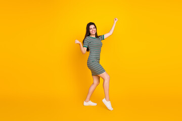 Attractive young girl in striped dress happily showcases casual style against vibrant yellow backdrop
