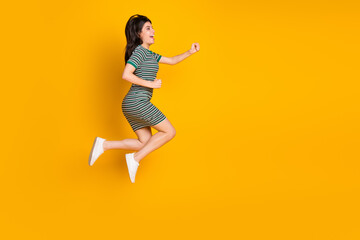 Charming young woman in striped dress jumping joyfully with a bright yellow background