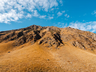 Rock mountain peaks on autumn hills on blue sky and cloud background on sunny day, walking view at Juta, Georgia. Brown and yellow colors of clean grass on small mountain, beauty landscape.