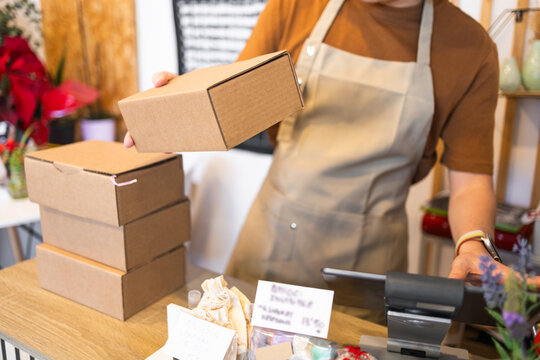 Retail worker packaging cardboard boxes at checkout counter - Powered by Adobe