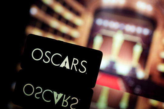 A smartphone displaying the Oscars logo against a blurred awards ceremony background.