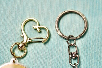 Key chain heart and round metal ring hook clip isolated on horizontal light blue background.
