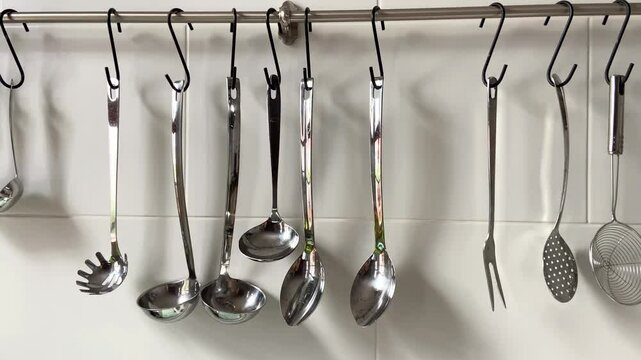 A set of cooking utensils on metal railing against a white ceramic tile wall in contemporary kitchen.Kitchenware,4K 
