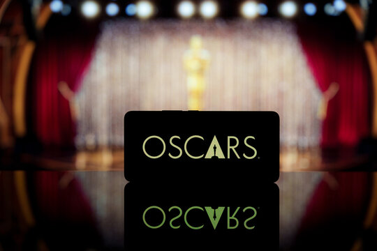 A smartphone displaying the Oscars logo against a blurred awards ceremony background.
