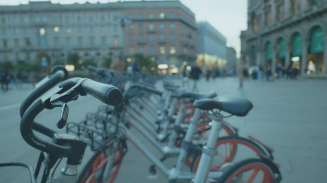 A row of bicycles parked in a lively urban square as dusk falls, highlighting the vibrant city life and the growing trend of cycling as a mode of transportation.