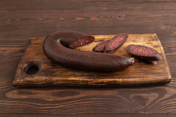 Sujuk sausage on wooden cutting board with pepper and herbs on brown wooden. Side view