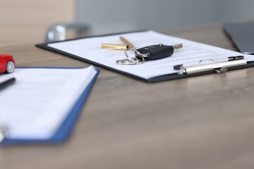 Car key and purchase agreement on wooden table, selective focus. Buying auto