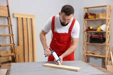 Worker with caulking gun glueing wooden plank indoors